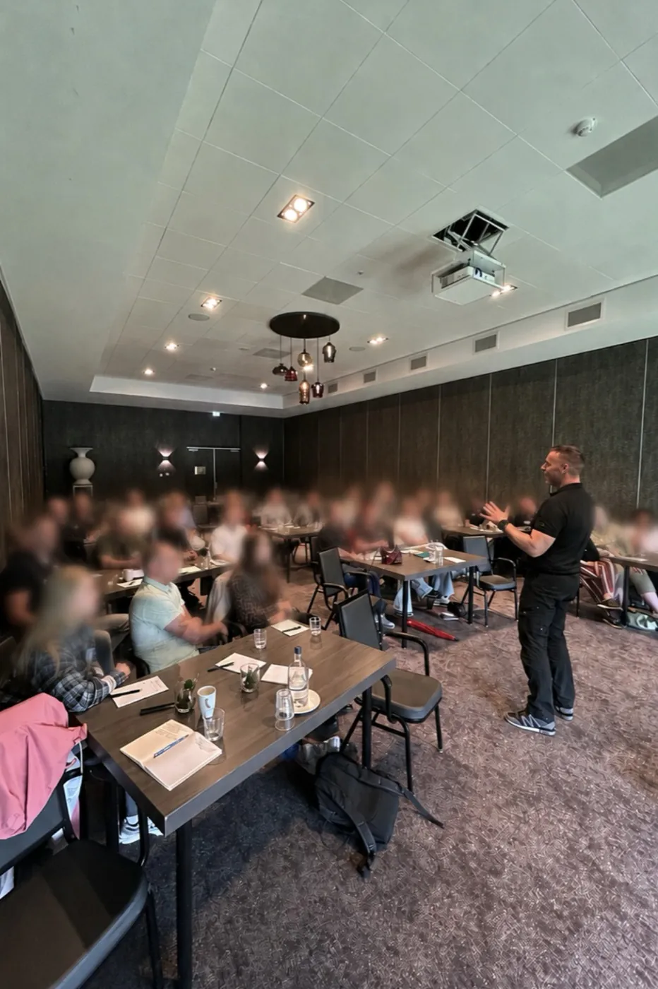 Maikel voor een groep deelnemers in een trainingsruimte