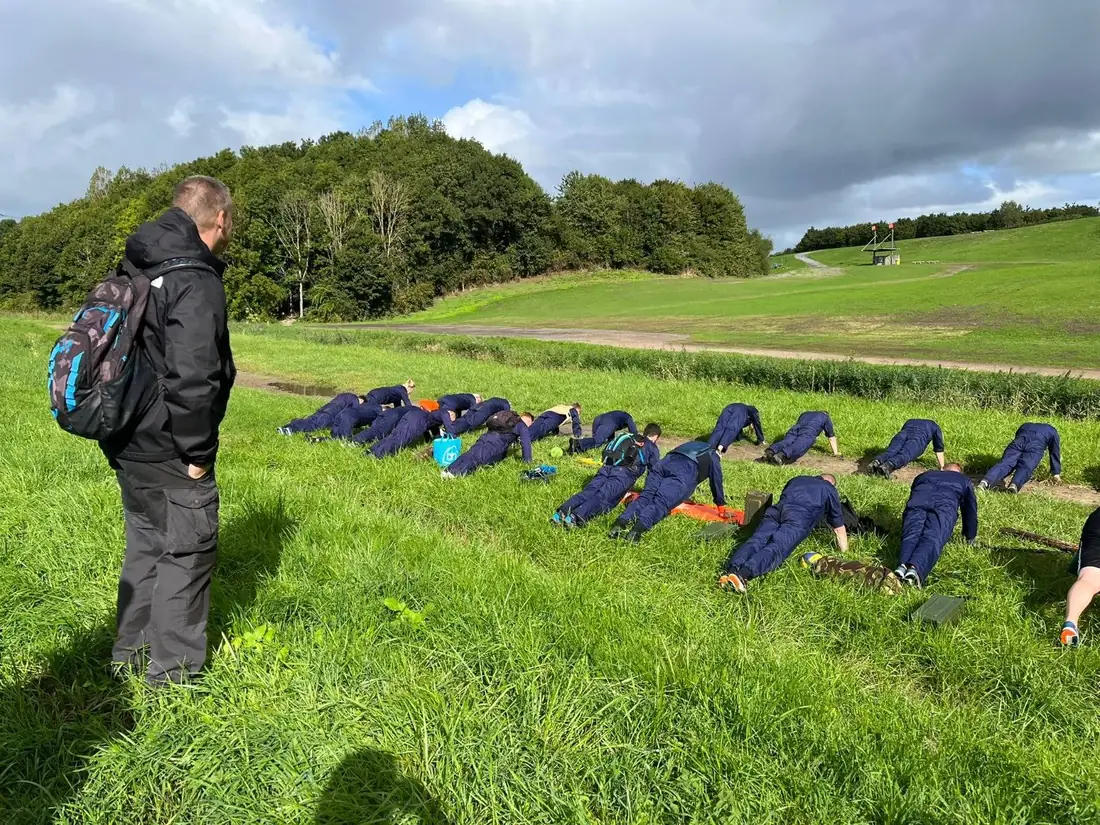 Maikel kijkt toe bij een buitentraining van een groep in overalls